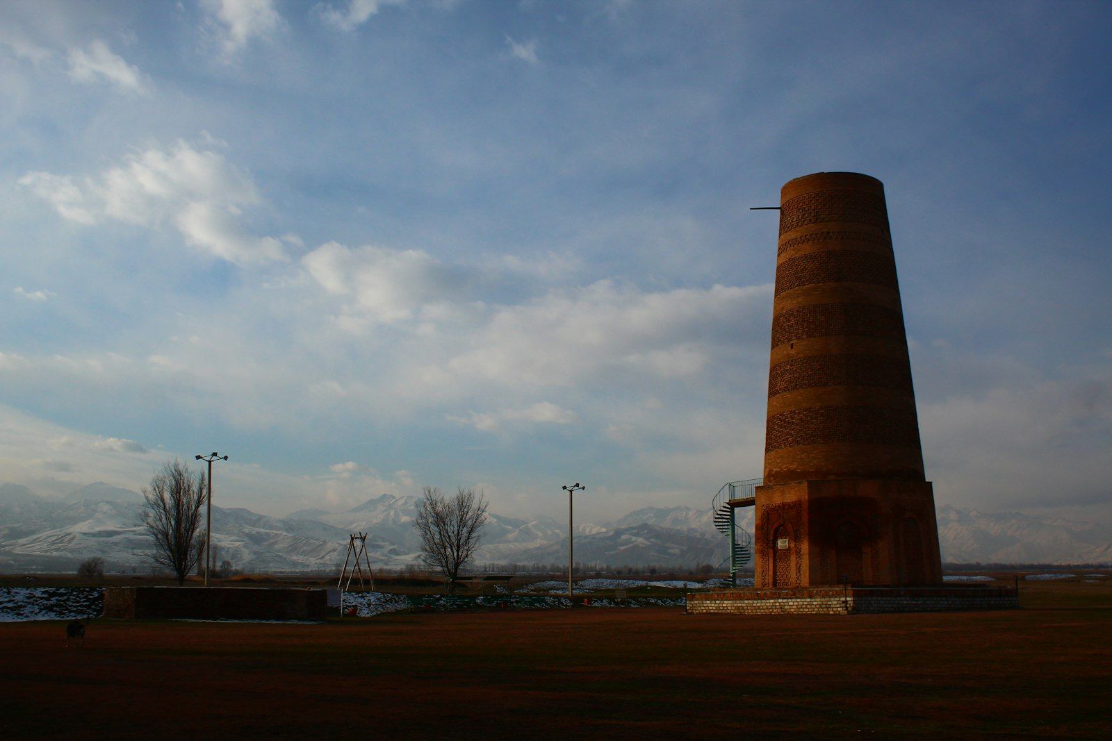 The brick minaret of Burana Tower rising from the grassy plain of ancient Balasagun, with the snow-dusted Tien Shan range beyond.