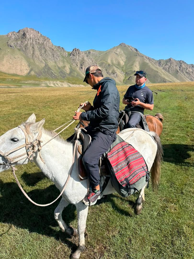 Two riders on horseback in a high mountain meadow.