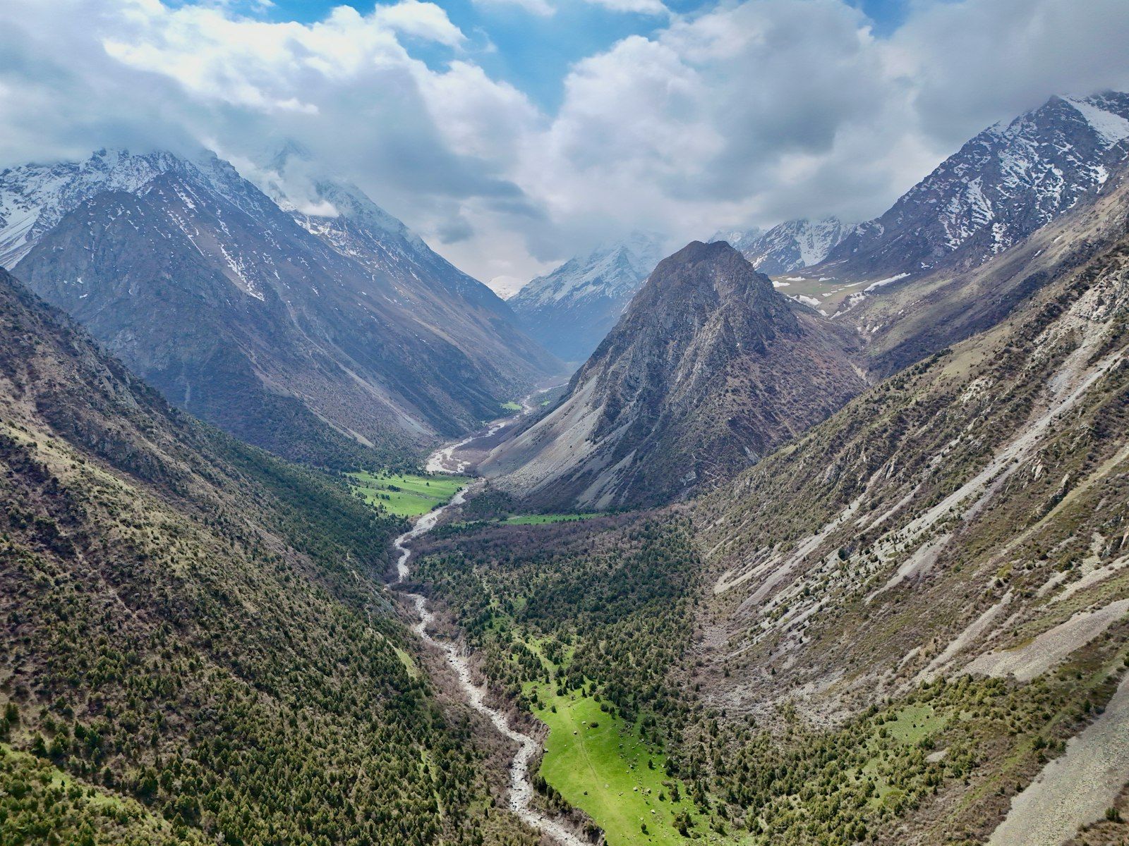 A broad glacial valley with a river winding between green slopes and snow-dusted peaks.