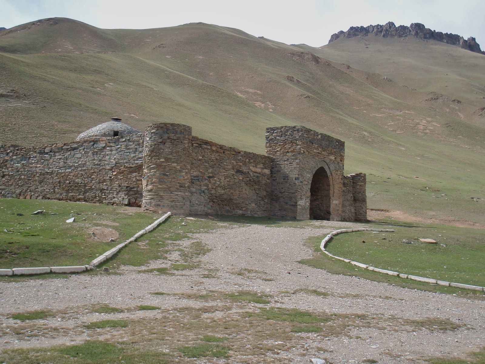 The stone Tash Rabat caravanserai set in a green high-mountain valley.