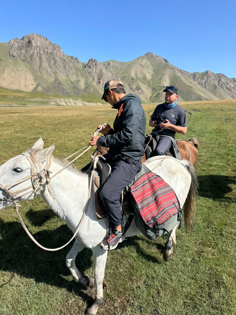 Two riders on horseback in a high mountain meadow.